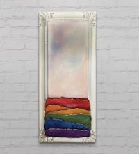 a painting of a rainbow in a white frame on a brick wall